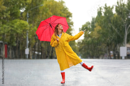 Happy young woman with red umbrella in city on rainy day