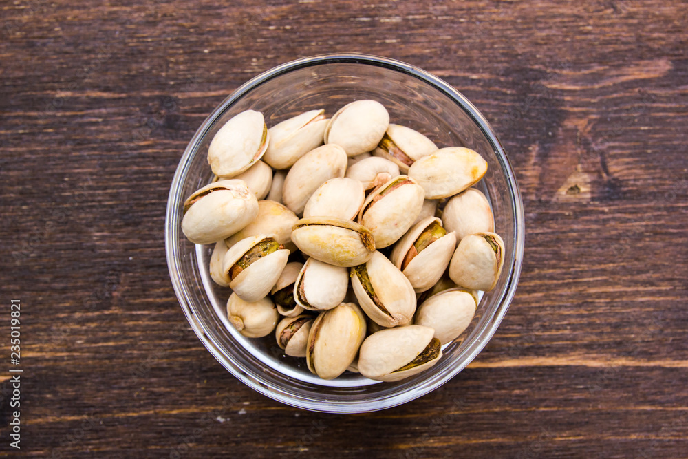 Pistachios on bowl on a wooden table viewed from above Pistachios on bowl on a wooden table viewed from above