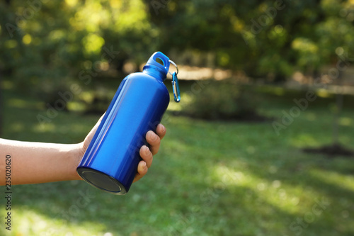 Young man holding bottle of water in park on sunny day, closeup. Space for text