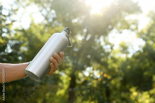 Young man holding bottle of water in park on sunny day, closeup. Space for text