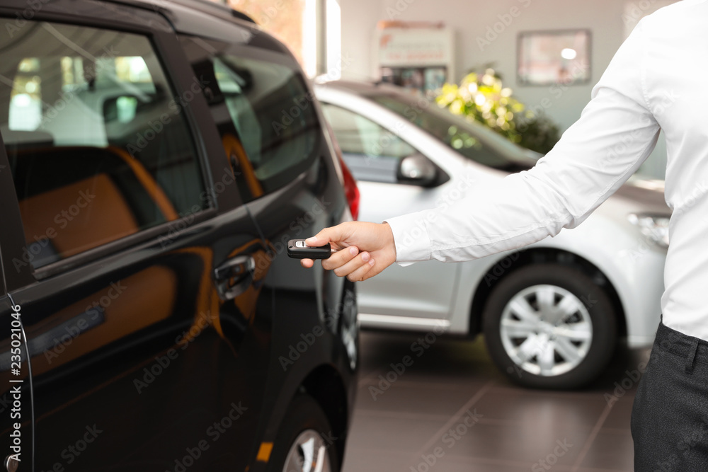 Young man turning off alarm system with car key indoors, closeup