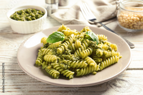 Plate with delicious basil pesto pasta on wooden table