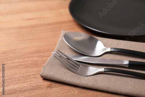 Table setting with cutlery, napkin and plate on wooden background, closeup