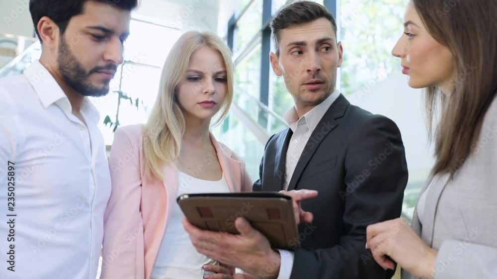 Multinational Group of Proggressive Startup Businesspeople using PC Tablet. The Head Showing New Project. They’re Standing in Big Bright Modern Office Building. Wearing Classic Suits.Teamwork.Business Multinational Group of Proggressive Startup Businesspeople using PC Tablet. The Head Showing New Project. They’re Standing in Big Bright Modern Office Building. Wearing Classic Suits.Teamwork.Business