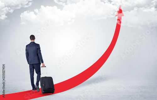 Young businessman with back leaving on the red arrow carpet to the skies with luggage on his hand 