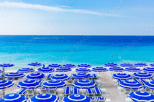 Blue umbrellas and chairs on beach by blue sea, in Nice, France
