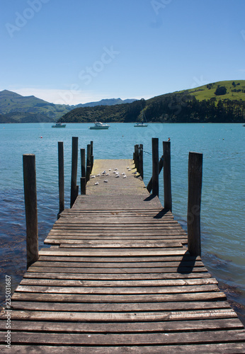 A wooden pier, sea and green hills in Akaroa near Christchurch in the South Island in New Zealand