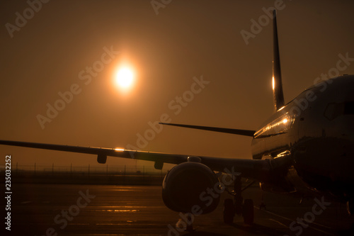 Large passenger aircraft shining in evening light waiting for flight on runaway illuminated by golden backlight sun low on the sky before sunset. Monochromatic yellow scene with empty space background