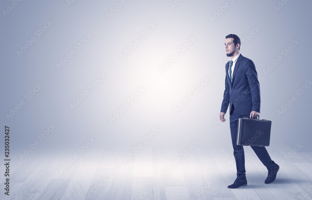 Successful businessman walking in front of an empty wall with briefcase on his hand
Successful businessman walking in front of an empty wall with briefcase on his hand