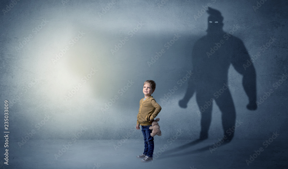 Cute kid in a room with plush on his hand and hero shadow on his background
