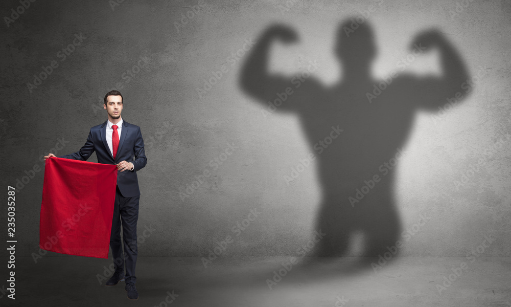 Fototapeta premium Businessman standing with red cloth on his hand and strong hero shadow on the background 