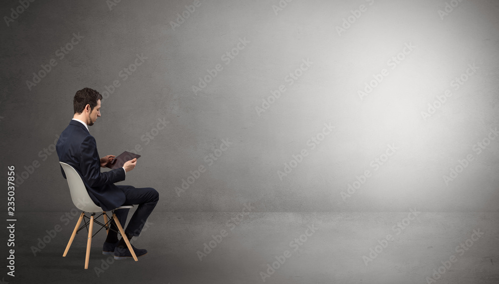 Businessman staying in an empty grey dark room with stuffs on his lap
