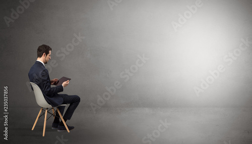 Businessman staying in an empty grey dark room with stuffs on his lap 