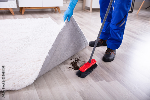 Fotografija Janitor Cleaning Dirt Under The Carpet