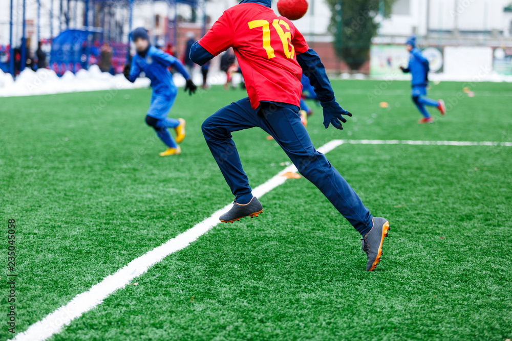 Boys in red and blue sportswear kicking soccer ball on green grass field. youth football game. Children sport competition, kids plays outdoor, winter activities, training Boys in red and blue sportswear kicking soccer ball on green grass field. youth football game. Children sport competition, kids plays outdoor, winter activities, training
