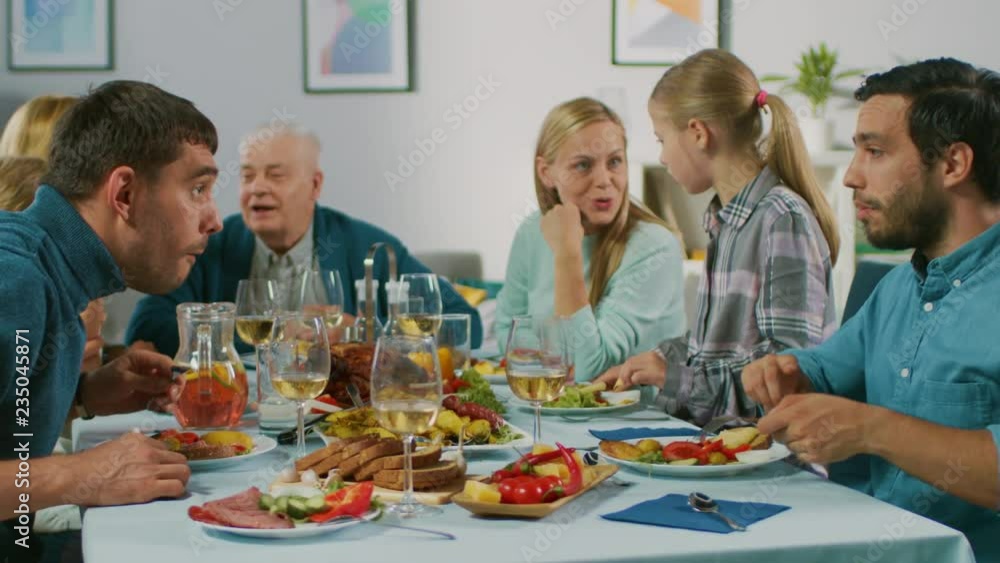 Big Family and Friends Celebration at Home, Diverse Group of Children, Young Adults and Old People Gathered at the Table. Eating, Sharing Meals, Drinking and Having Fun Conversation. In Slow Motion. Big Family and Friends Celebration at Home, Diverse Group of Children, Young Adults and Old People Gathered at the Table. Eating, Sharing Meals, Drinking and Having Fun Conversation. In Slow Motion.
