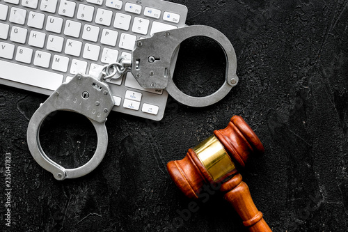 Arrest of a hacker for cyber fraud concept. Handcuff near keyboard and judge gavel on black background top view