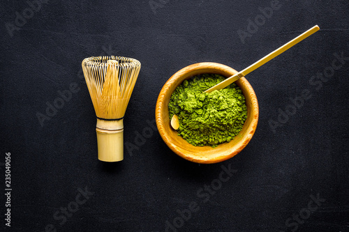 Japanese matcha tea tradition. Matcha accesories, whisk near matcha powder in bowl on black background top view copy space