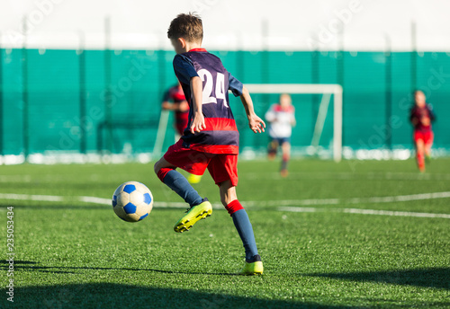 Young Active sport heathy boys in red and blue sportswear running and kicking a red ball on football field with artificial turf. soccer youth team plays football. activities for kids, training © Natali