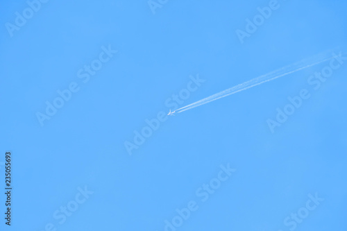 Airplane flying with white contrail in the blue sky. Minimal background.