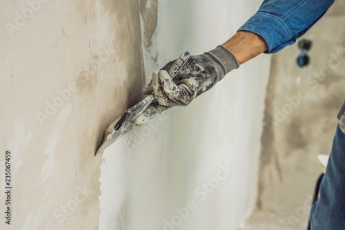 master is applying white putty on a wall and smearing by putty knife in a room of renovating house in daytime