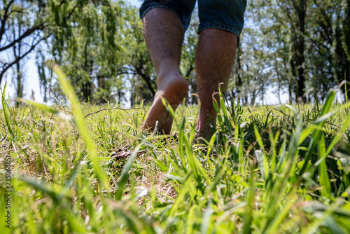 Man with jean shorts walking away on green grass and trees on the back