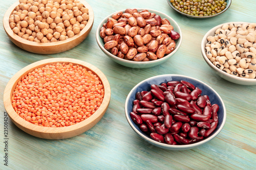 Various types of legumes on a teal background. Red kidney beans, lentil, chickpea, soybeans, black-eyed peas