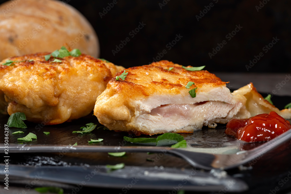 Two pieces of cordon bleu on a dark slate with a chopped green parsley