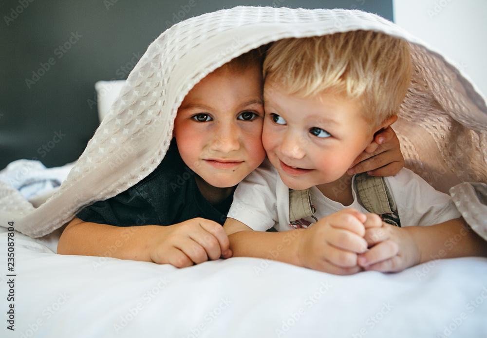 Brothers play together.Two boys brothers lie under a blanket in bed. Brothers play together.Two boys brothers lie under a blanket in bed.