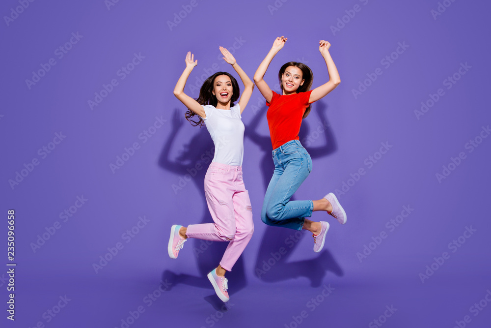 Two charming lovely cute dreamy girls jumping up raising hands isolated violet purple background Two charming lovely cute dreamy girls jumping up raising hands isolated violet purple background