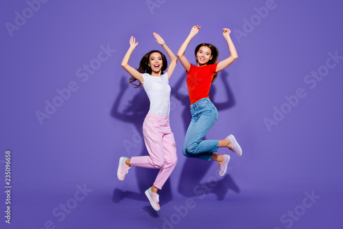 Two charming lovely cute dreamy girls jumping up raising hands isolated violet purple background