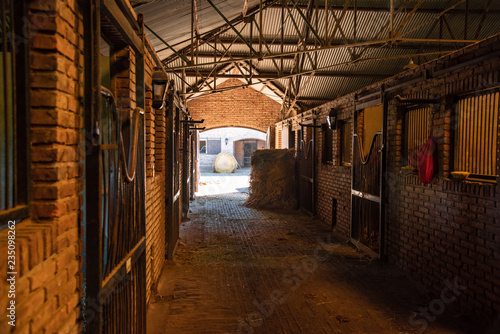 Inside a bricks stable looking trough a door  two hay rolls and horses stals