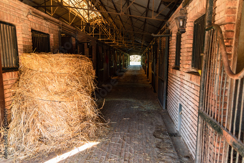 Inside a bricks stable with a lot of horses stals and a hay bale