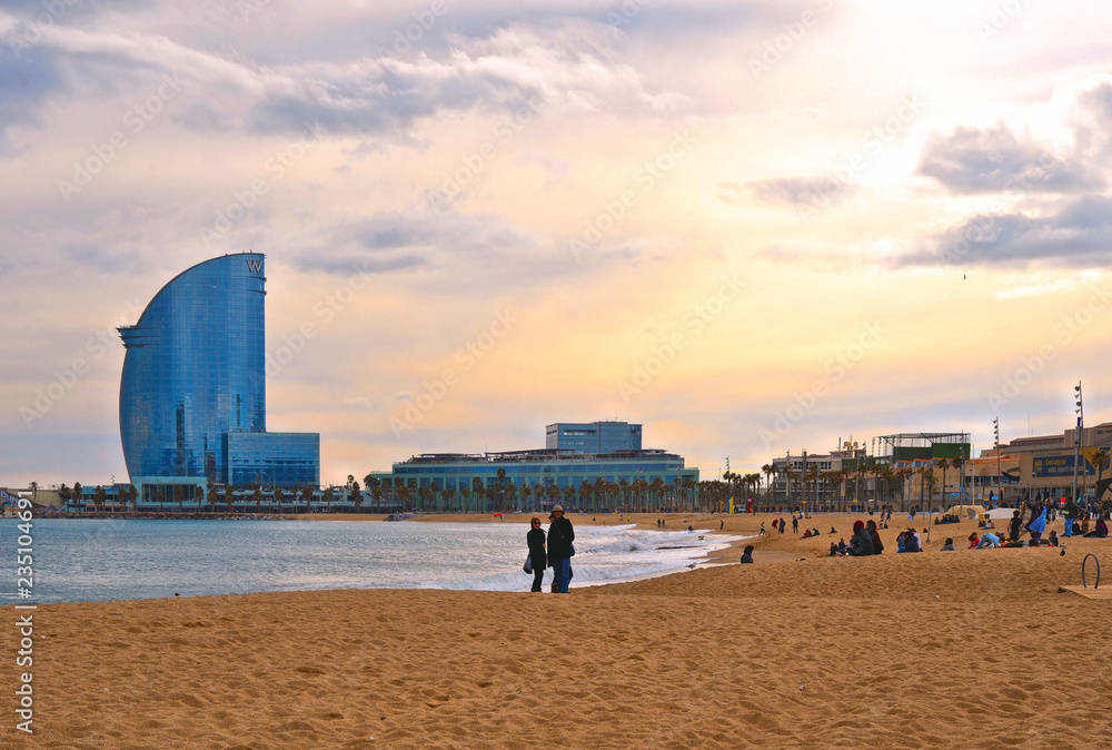 city beach Barceloneta with peoplea and modern architecture and cloudy sky in background in Barcelona, Spain