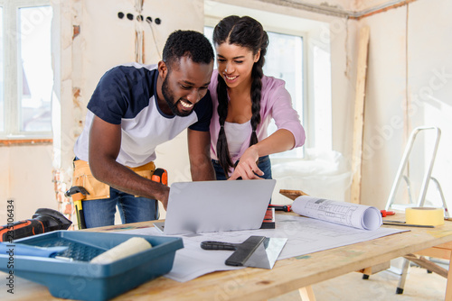 young african american woman pointing at laptop screen to boyfriend during renovation of home
