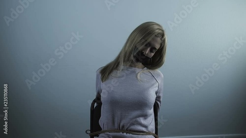 Unconscious blond woman taped mouth sitting chair tied with ropes, kidnapping photo