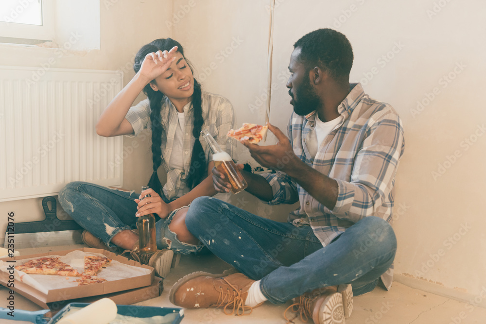 tired young couple with beer and pizza sitting on floor while making renovation of home