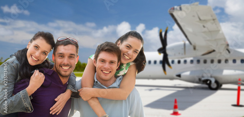 tourism, travel and people concept - group of happy friends over plane on airfield background