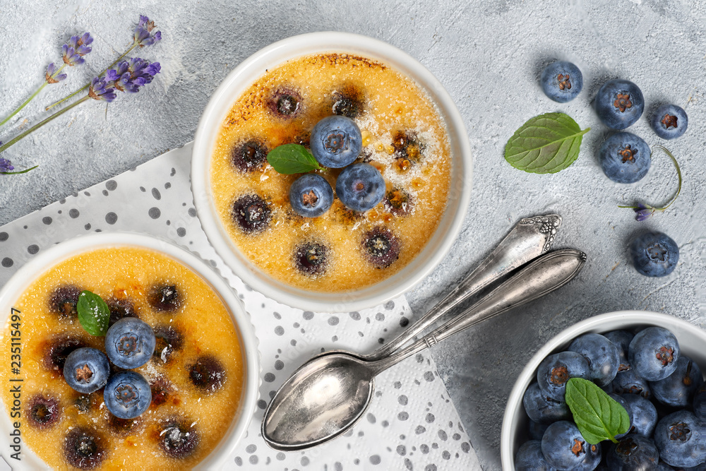 Creme brulee with blueberry and lavender powdered with sugar on light concrete background Creme brulee with blueberry and lavender powdered with sugar on light concrete background
