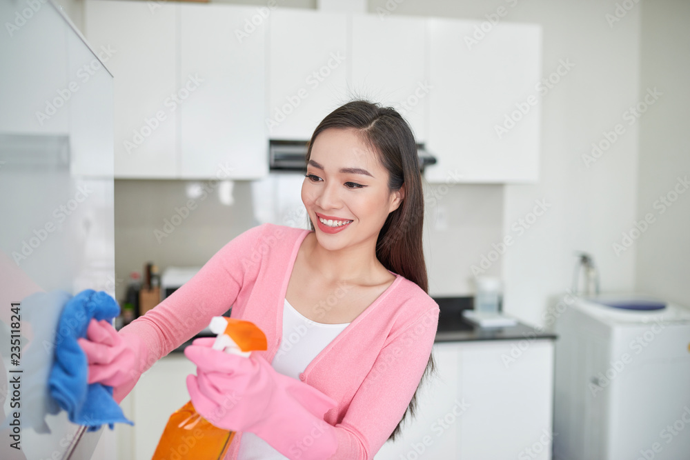 Woman in protective gloves cleaning refrigerator with rag indoors Woman in protective gloves cleaning refrigerator with rag indoors