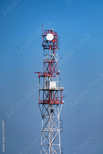 View of red and white communication tower against blue sky