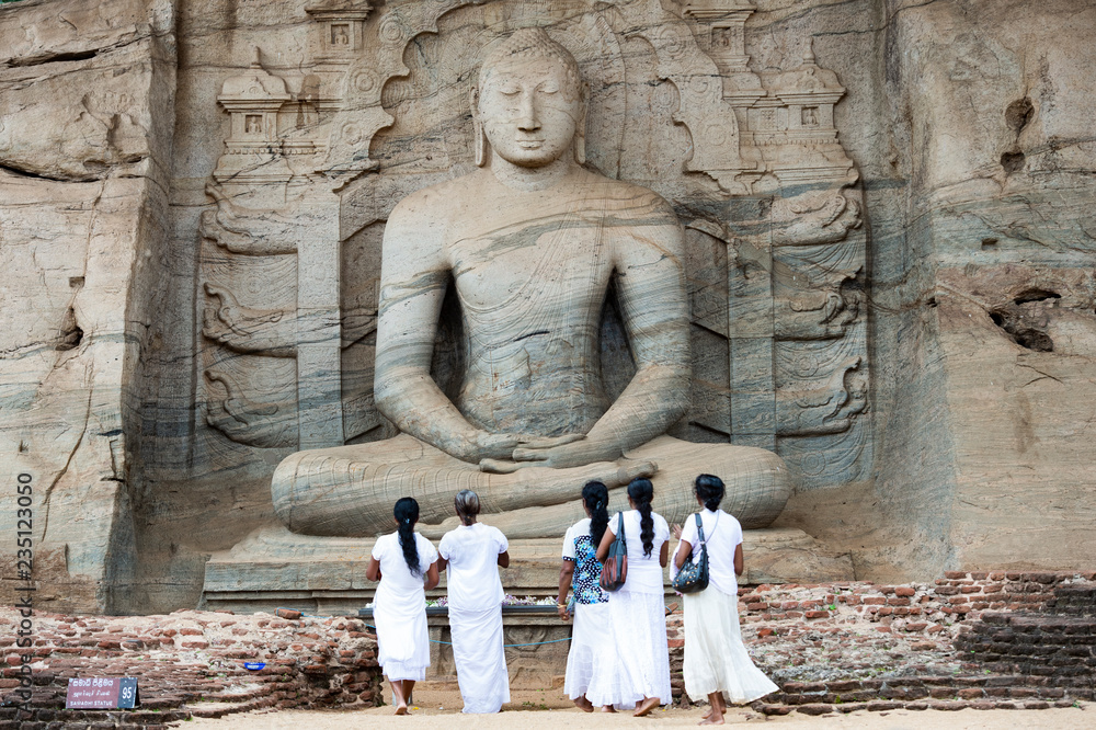 Five religious women are standing and admiring the great Samadhi Statue in Polonnaruwa, Sri Lanka.