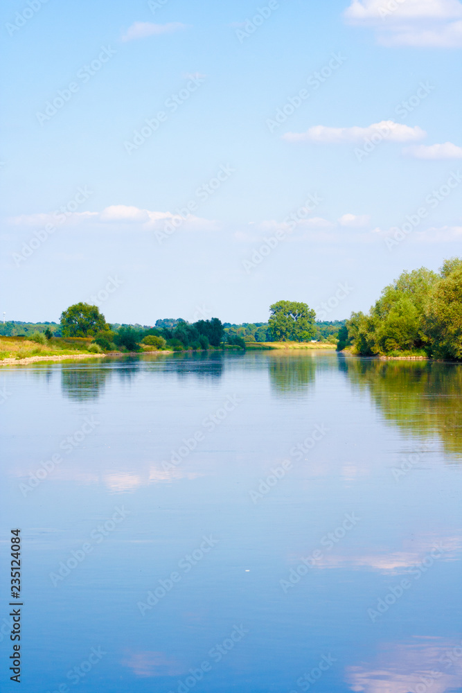 A beautiful river landscape. Flowing river that reflects the sky and plants on the shore. The shore is lined with stones.