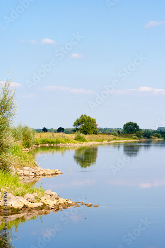 A beautiful river landscape. Flowing river that reflects the sky and plants on the shore. The shore is lined with stones.