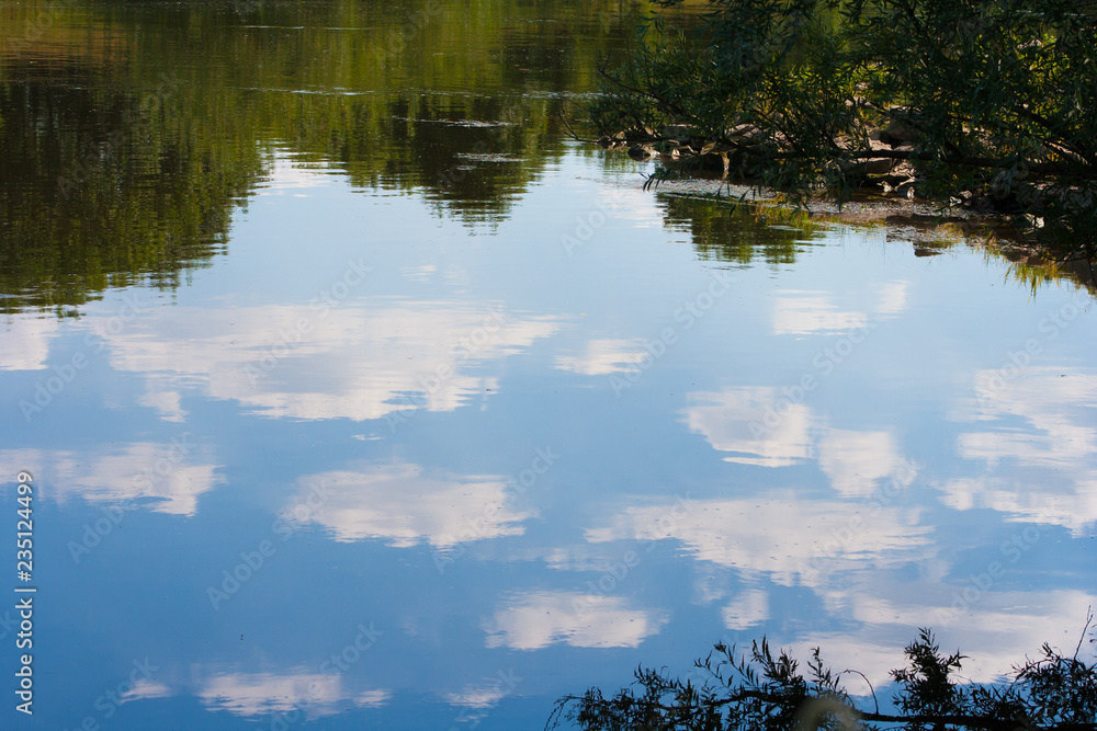 White clouds are reflected from the water's surface. The river reflects a beautiful landscape