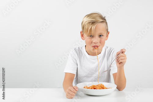 little blond boy in front of white background eats spaghetti 