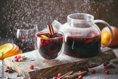 homemade mulled wine with cranberries in glasses and teapot with falling powdered sugar on table in kitchen