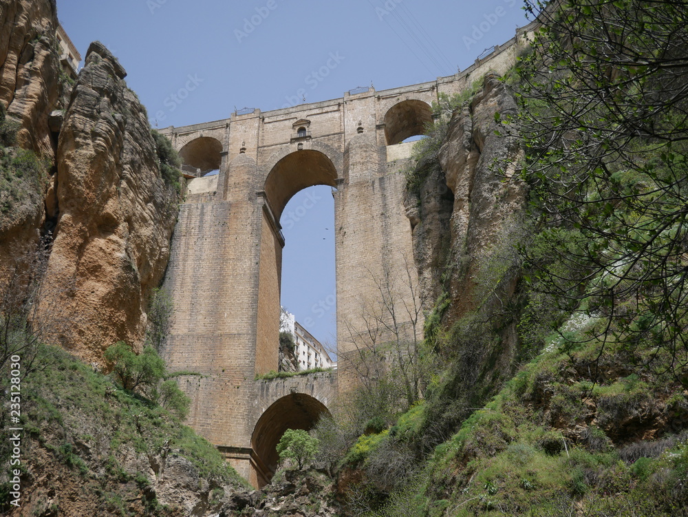 Old bridge connecting two parts of a city over a canyon in the mountains of Ronda, Spain, seen from below