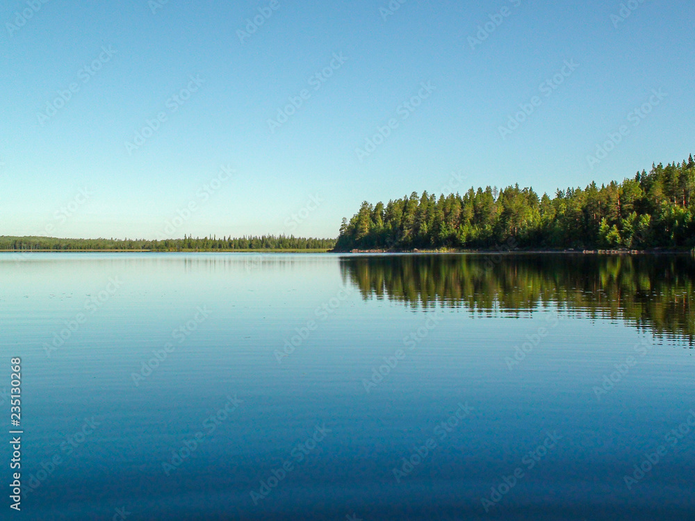 Blue lake as a mirror for green forest and blue sky Blue lake as a mirror for green forest and blue sky