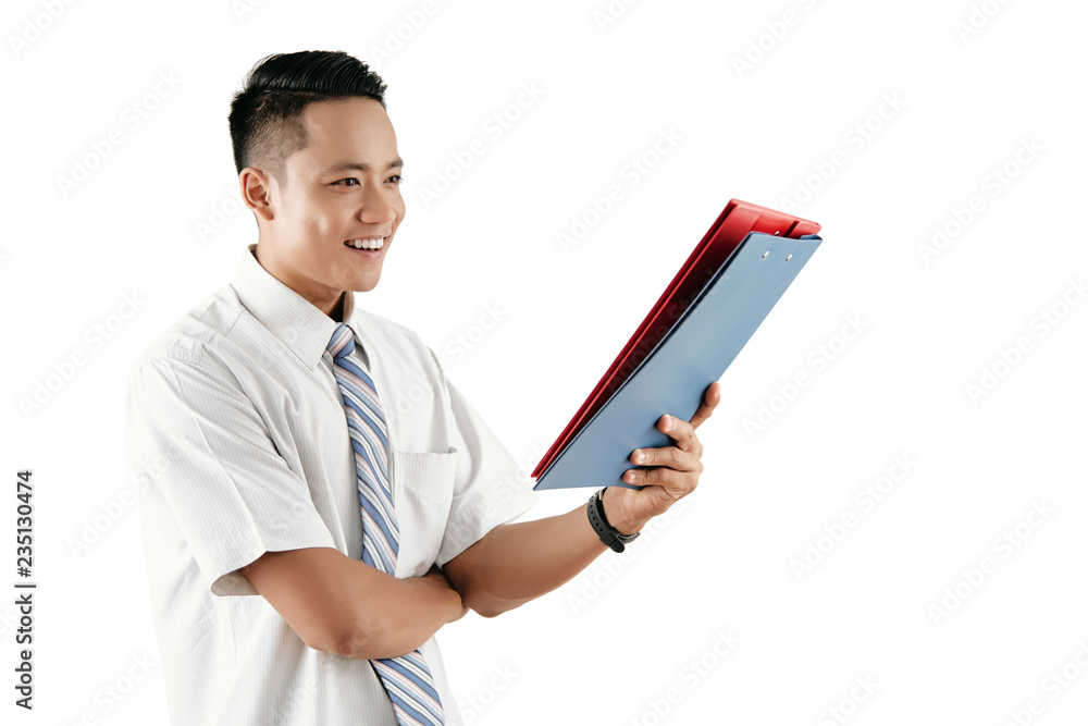 Young attractive Asian male office worker looking at folders with papers and smiling joyfully while standing against white background Young attractive Asian male office worker looking at folders with papers and smiling joyfully while standing against white background